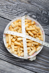 A cup with crackers. Wrapped crosswise with measuring tape. On brushed pine boards. View from above. Symbol of World No Diet Day.