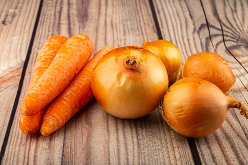 Juicy ripe onions and orange carrots on a wooden background. Close up.