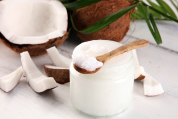Coconut oil with fresh nut and palm leaves on rustic background.