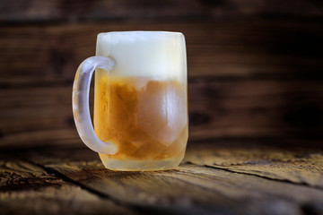 Big bright beer in frozen glass on the old wooden table as a background...