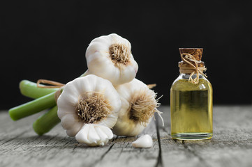 Glass bottle of garlic oil  and Ripe and fresh garlic plant on wooden or rustic table, alternative...
