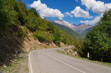 Fototapeta premium Scenic empty road in the mountains of the Caucasus. View of the snowcapped peak of the Ushba Mountain. Nature and travel. Georgia, Svaneti region