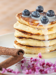 stacked pancakes with caramel syrup and blue berries with cinnamon sticks on wooden paper