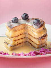 stacked pancakes with caramel syrup and blue berries with cutted piece on pink background
