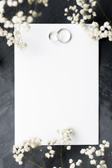 Gypsophila branches and white gold wedding rings for a card or wedding invitation. White sheet of paper for inscription on a gray background, copyspace