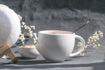 delicate breakfast cottage cheese with jam in a white cup, pumpkin seeds, eco air humidifier, a beautiful and healthy meal in the bright sun on a gray background with gypsophila flowers