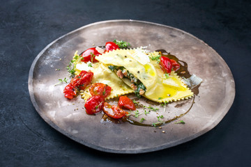 Traditional Italian ravioli pasta offered with salmon spinach filling and fried tomatoes as closeup on a modern design plate