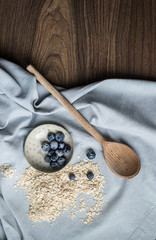 Top view of a breakfast set up: blueberries, oat flakes and a wooden spoon.