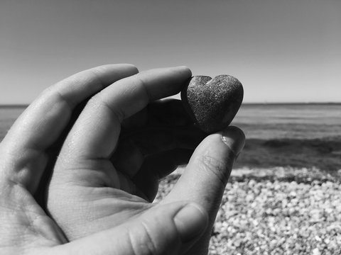 Cropped Hands On Couple Holding Heart Shape Stone At Beach