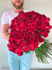 Bearded man in white t shirt holding in hands rich gift bouquet of 101 red roses