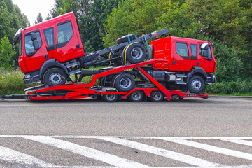 Truck carrier trailer transporting two brand-new trucks of red color.   