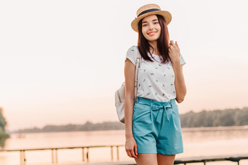 Beautiful young woman walking on pier at sunset in summer.