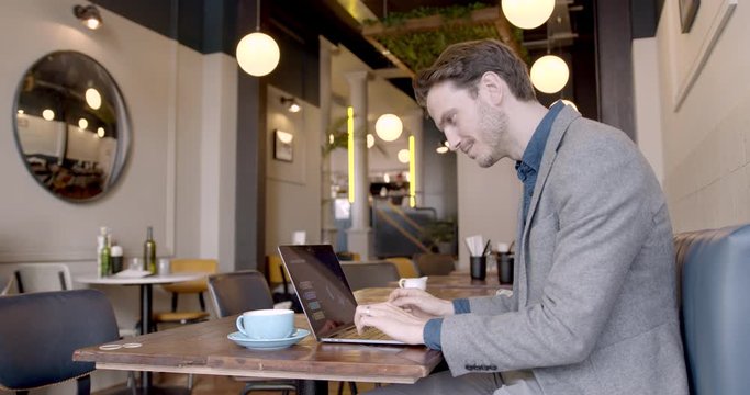 Businessman sitting and working in empty cafe restaurant on laptop. Man using computer devices and wireless technology. Business and entrepreneurship