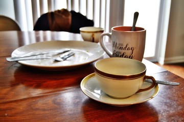 Dirty plate with knife and fork and couple of cups left after lunch on the table