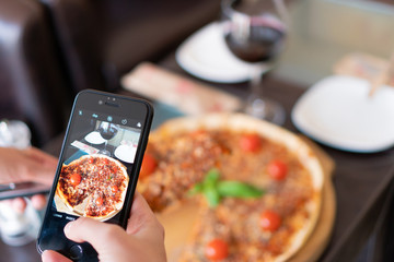 a girl taking photo of pizza with a glass of wine in the background