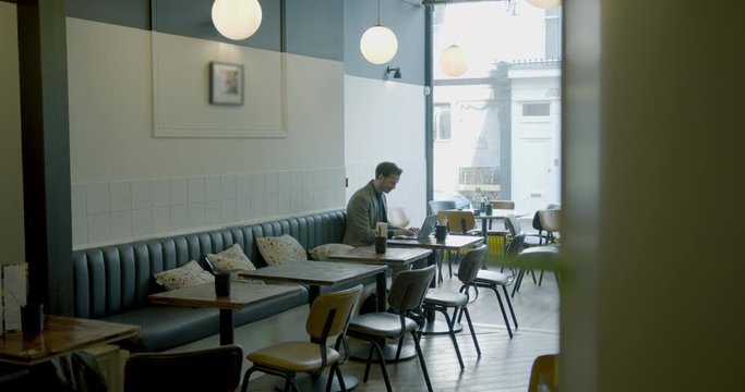 Businessman sitting and working in empty cafe restaurant on laptop. Man using computer devices and wireless technology. Business and entrepreneurship