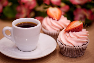 Chocolate cupcakes with strawberries. Cupcakes and a cup of coffee on the table with flowers. Selective focus.