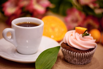 Chocolate cupcakes with kumquat. Cupcakes and a cup of coffee on the table with flowers. Selective focus.