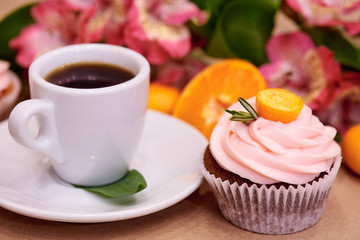 Chocolate cupcakes with kumquat. Cupcakes and a cup of coffee on the table with flowers. Selective focus.