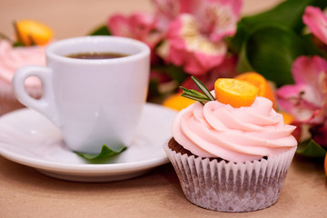 Chocolate cupcakes with kumquat. Cupcakes and a cup of coffee on the table with flowers. Selective focus.