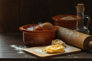 Homemade pasta on a Board with flour and ingredients for cooking on a dark wooden background