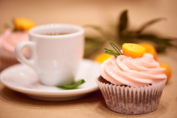 Chocolate cupcakes with kumquat. Cupcakes and a cup of coffee on the table with flowers. Selective focus.