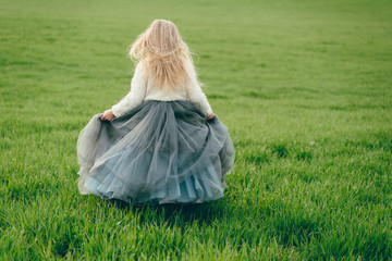 little princess with blond hair in a luxurious gray dress on a background of green field. Princess day.