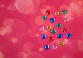 Colorful heart shape rhinestones crystals as pattern on pink background.
