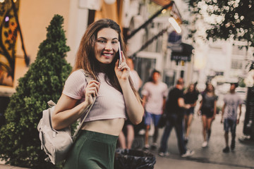 Fototapeta premium Smiling woman using phone and drink coffee on the street in summer day.