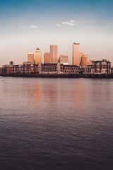 Fototapeta premium Canary wharf banking center by the majestic river at sunset with old buildings London Vertical