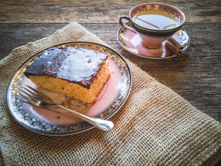Plate with chocolate covered cake and cup of tea. Rustic wood background.