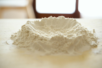 Staying at home with your family and preparing fresh home-made pasta (tagliatelle): flour on a wooden surface with a hole in the middle where to put the eggs, volcano shaped.