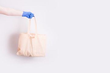 a hand in a blue disposable medical rubber glove holds a shopping bag for shopping, light background, copy space, contactless delivery concept, self-isolation and quarantine, light background.
