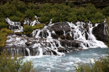 Fototapeta na wymiar Hraunfossar / Iceland - August 15, 2017: Hraunfossar waterfalls formed by rivulets streaming out of the Hallmundarhraun lava field formed by the eruption of a volcano lying under the glacier Langjokul