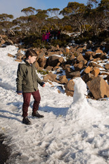 Young boy destroying a small snowman he by kicking it down