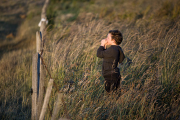 Naklejka na ściany i meble Young boy standing in long grass near a farm fenceline