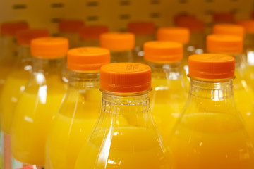 A lot of plastic bottles with orange juice on a store shelf. Close-up