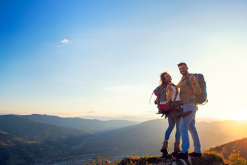 happy couple man and woman tourist at top of mountain at sunset outdoors during a hike in summer