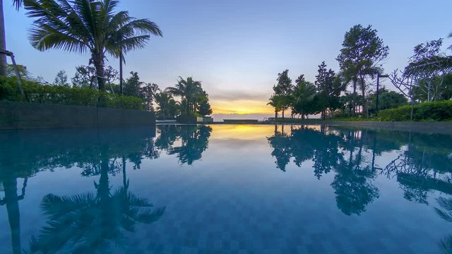 4K time lapse of beautiful sunrise at swimming pool with tropical trees and large reflection.