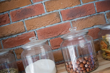 Walnuts, pasta,grains and salt in glas jars in modern loft design kitchen in front of bricked wall, cooking concept