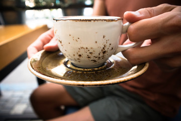 a young handsome man is sitting  in a cafe with friends and drinking hot cappuccino ,relaxing, close up of a cup