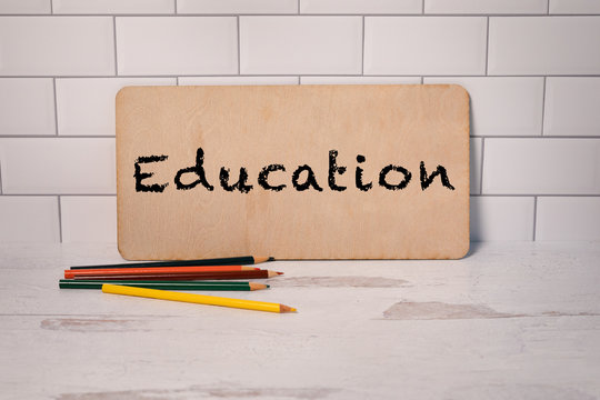 The word Education painted in black on a wood board coloring pencils laying on the table next to sign education industry 