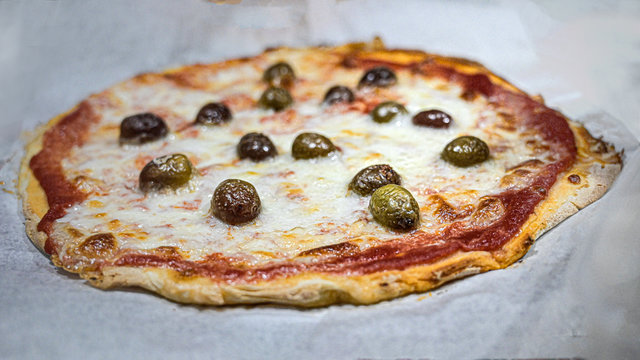 preparazione di una pizza fatta in casa con pomodoro, mozzarella, olive, capperi e olio extra vergine d'oliva