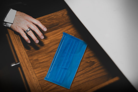 Close Up Hand Of A Business Man Is Picking A Blue Mask In The Drawer Under The Desk, Wearing It To Protect Coronavirus (covid-19) And Looking After His Own Health.