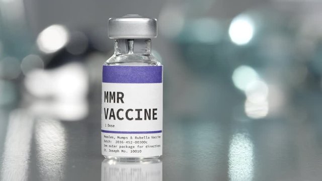 MMR measles, mumps, and rubella vaccine vial in medical lab with syringe placed next to it.
