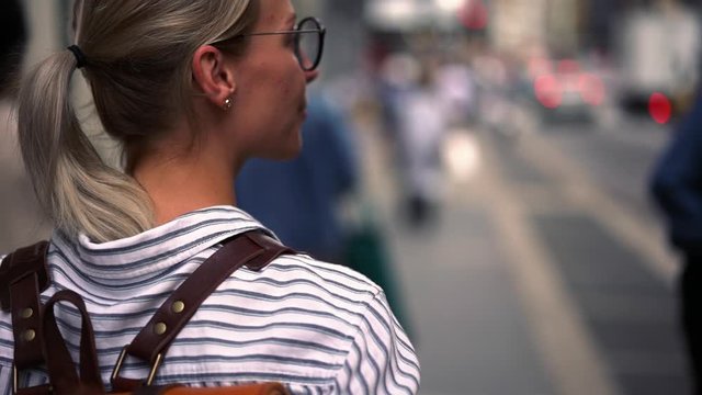 Slow motion effect with back view of young beautiful hipster girl with leather travel backpack enjoying walking around urban setting during touristic vacations. Female woman wanderlust exploring city
