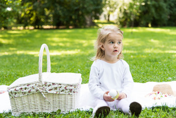 A little beautiful girl walks in the park with a picnic basket and straw hat. Funny emotional baby.