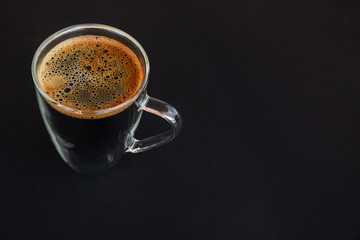 A glass cup of black coffee on a black background
