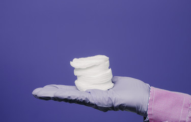 A guy in a medical glove holds cotton pads. Violet background. Medical and cosmetology content