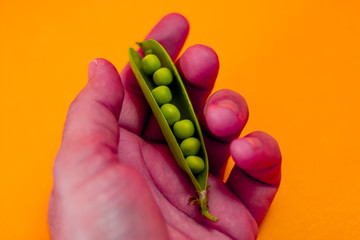 man holding red painted hand and green peas over orange background